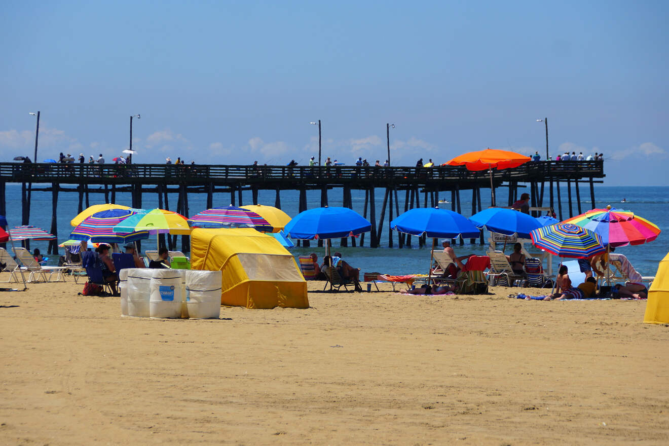 A vibrant beach scene at Virginia Beach with colorful umbrellas and beachgoers enjoying the sunny weather on the sandy shore near a fishing pier